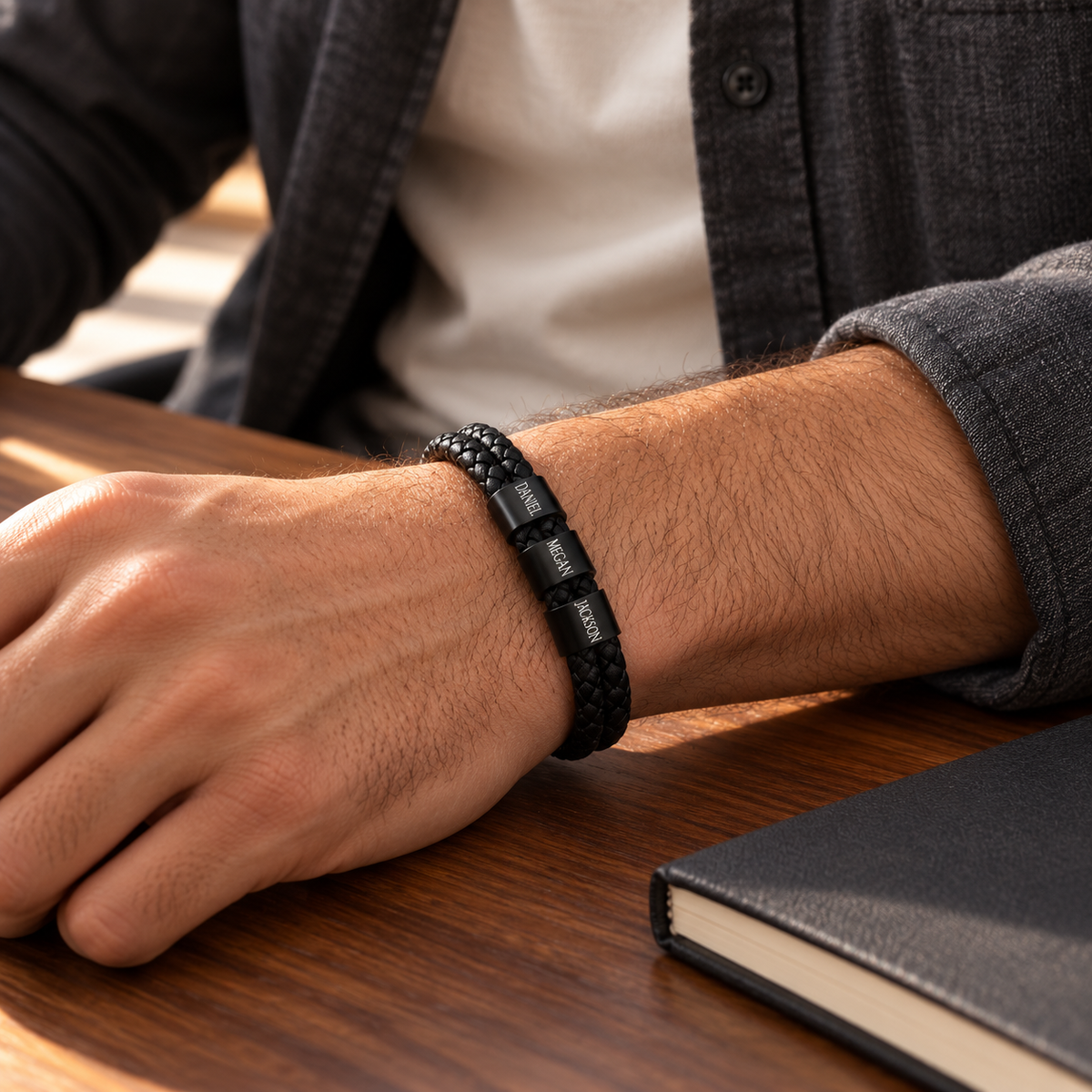 Man wearing a personalized black braided leather bracelet with engraved name rings on his wrist.
