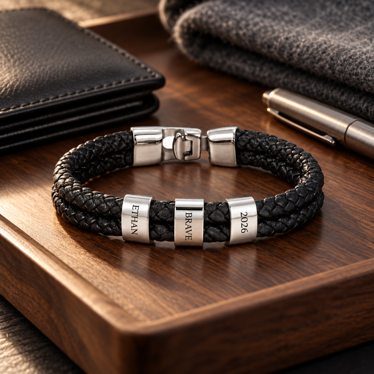 Personalized silver-finish braided bracelet displayed on a walnut valet tray with a leather wallet and pen.
