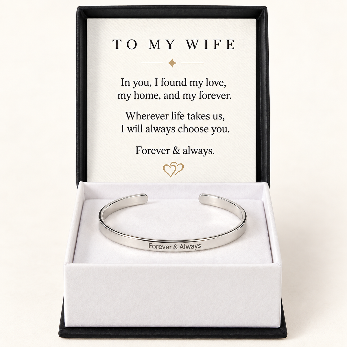 A silver open cuff bracelet engraved with 'Forever & Always' presented in a white gift box with a black outer frame. The inside lid features a printed message addressed 'TO MY WIFE'.