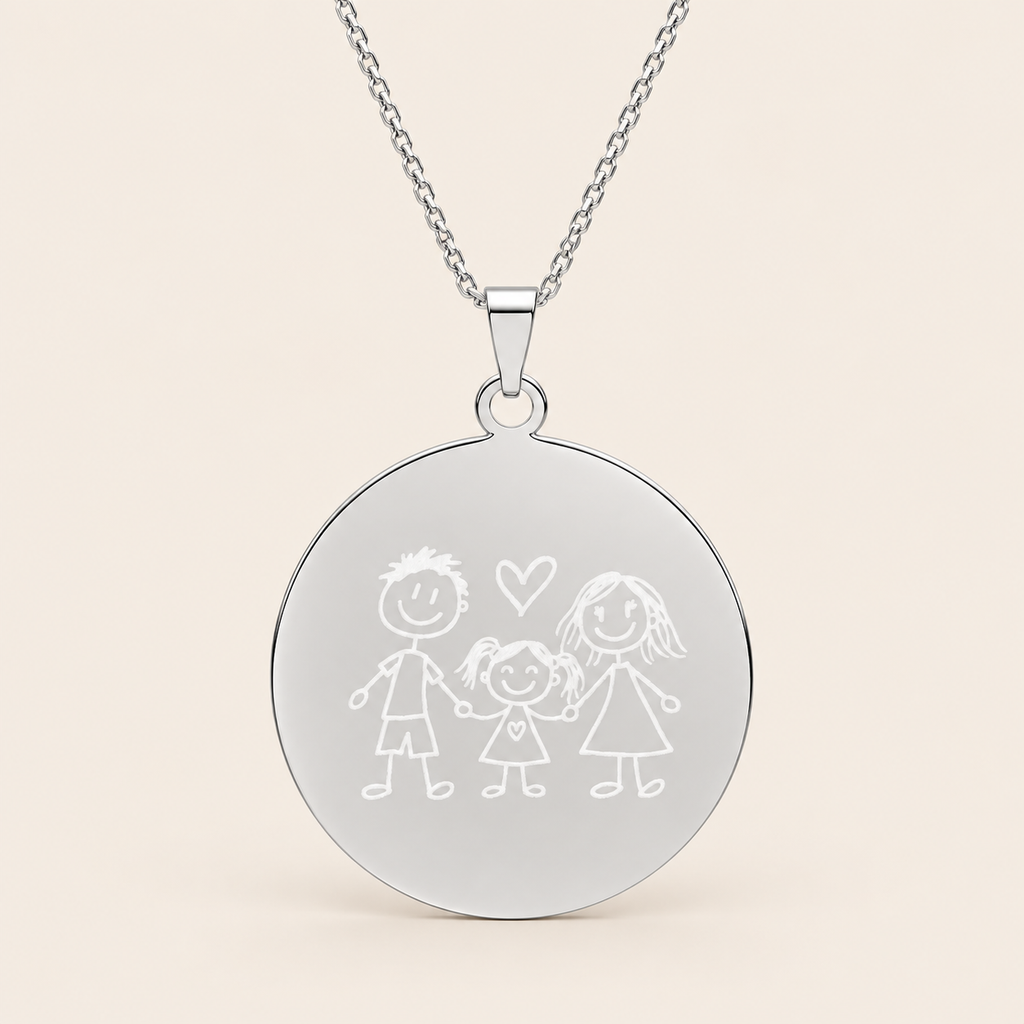 A silver round pendant necklace featuring a simple engraved stick figure family design with a small heart, suspended from a delicate silver chain against a light beige background.
